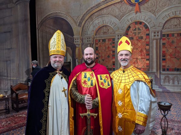Three Masons dressed in costume pose on a production set